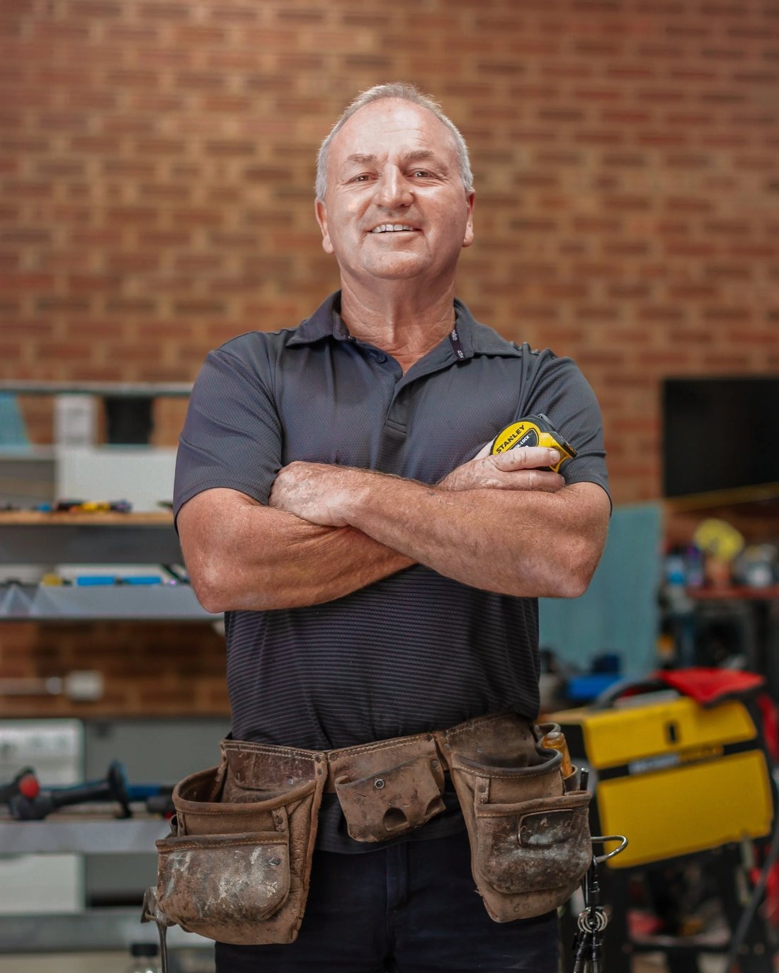 Gavin, founder of Barry, standing in his workshop wearing a leather tool belt with arms crossed