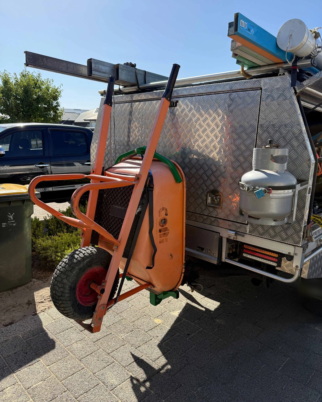 Customer setup: orange wheelbarrow carried on the tow hitch of a tradesman's ute canopy using Barry