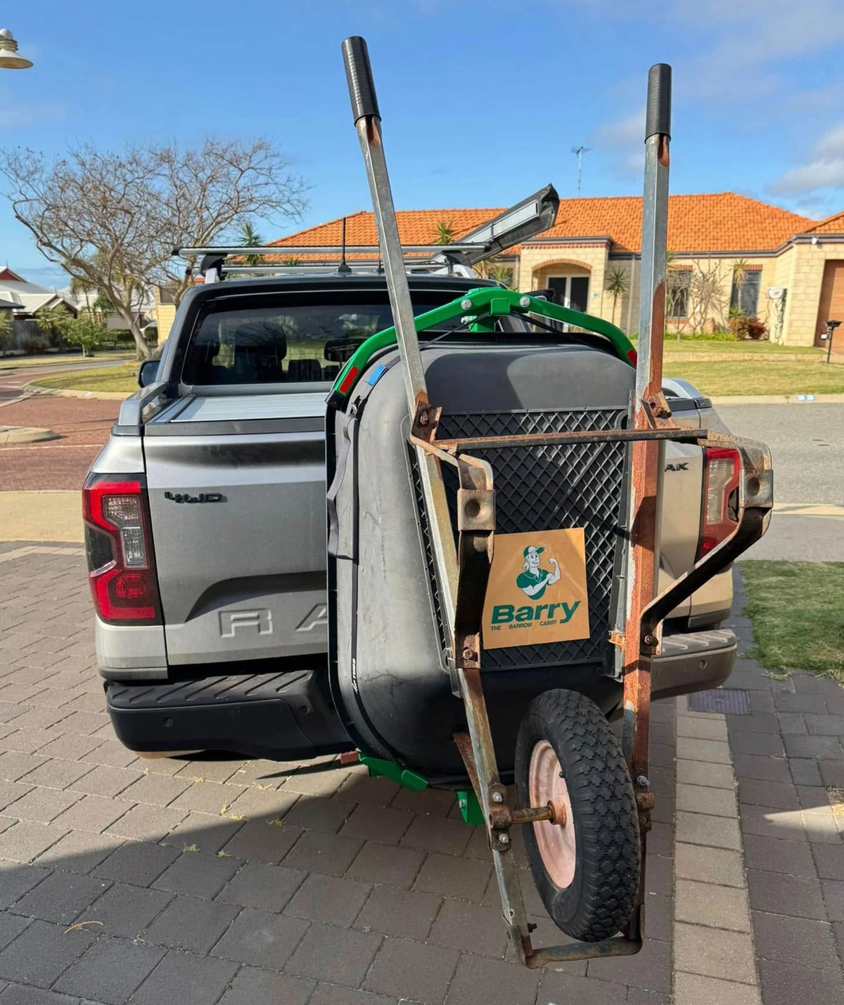 Barry wheelbarrow carrier mounted to a Ford Ranger tow hitch, holding a wheelbarrow upright behind the tailgate